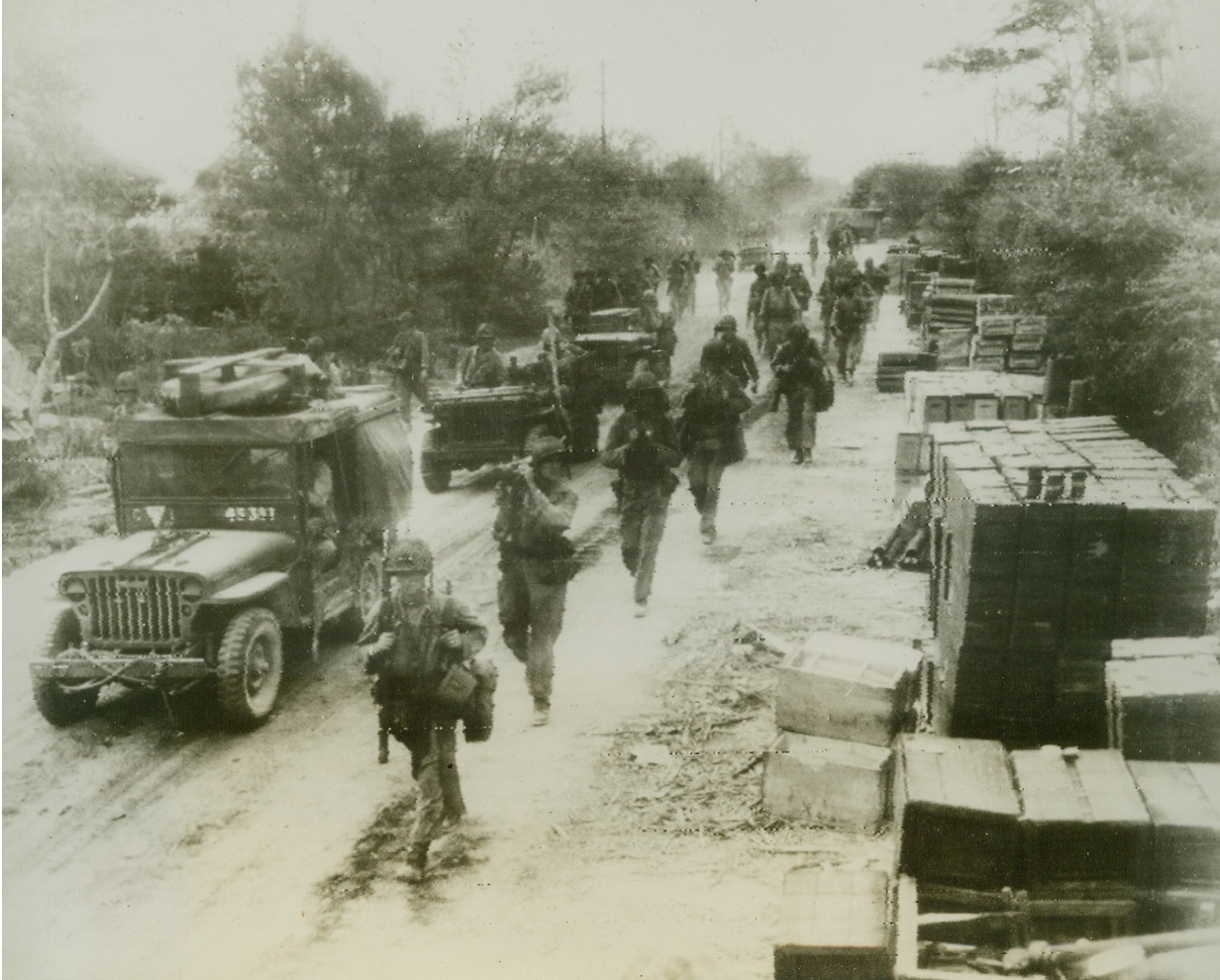 Yanks Move Up On Saipan Front, 6/24/1944. SAIPAN, M.I.—Along a Saipan road lined with ammunition cases, American troops and trucks move up to the front lines to reinforce leathernecks and doughboys engaged in bitter fighting for the vital Jap base. Photo radioed from Honolulu. Credit: ACME;