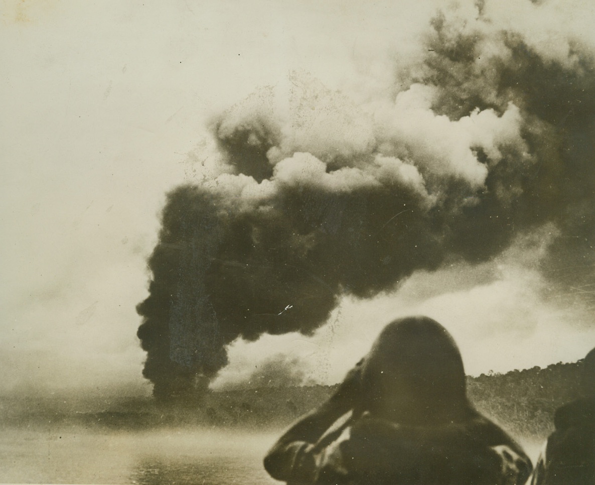 As Yanks Prepared Biak Landing, 6/14/1944. Columns of dense, black smoke rise from burning installations on tiny but strategic Biak Island in the Netherlands Indies, as U.S. Navy ships pound the Jap base as a part of landing operations last May 27th.  In the foreground a lookout carefully scans the skies watching for enemy planes which might use the smoke for cover in a strafing dive. Credit line (U.S. Navy photo from ACME);