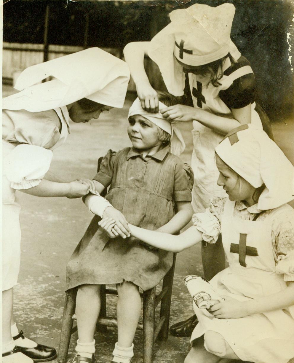 Youthful pill-pushers, 6/19/1944. ENGLAND – Dolls and building blocks have no lure for the young children at school in Beddington, Surrey. The study of first aid occupies all their time, and the youngsters are given instruction in the rudimentary functions. Here, three earnest little nurses attend a “patient”. Left to right: Ann Moon, 6; Patient Janet North, 5; Julia Walls, 7’ and Sheila Webb, 6. CREDIT (ACME) 6/19/44;