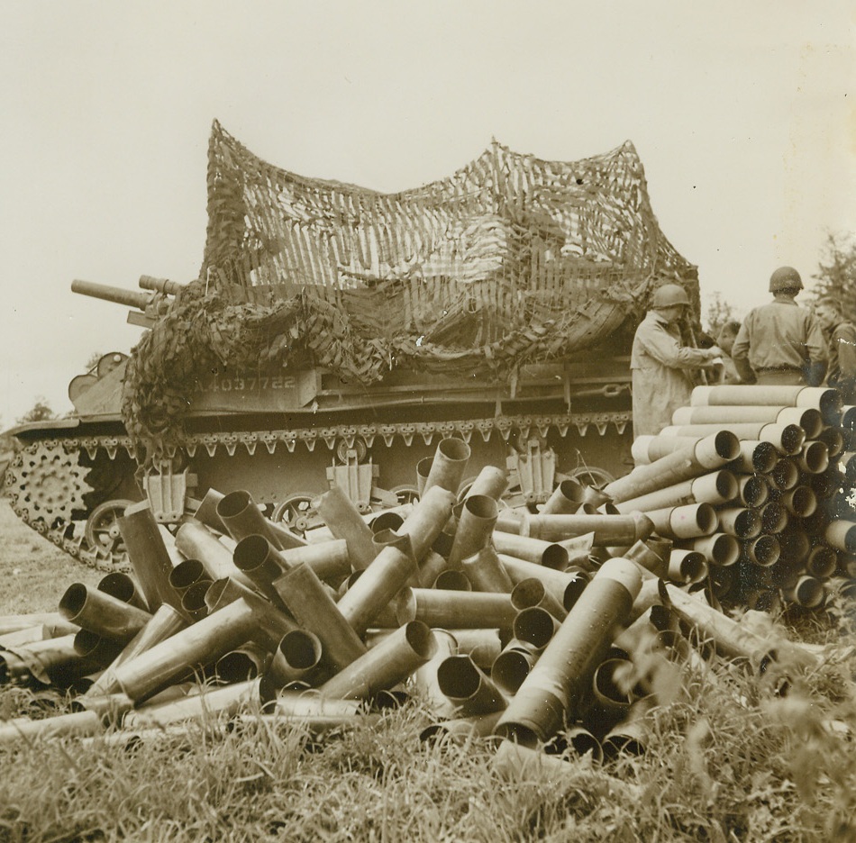 A Good Night’s Work, 6/19/1944. Carentan Area -- Piled helter-skelter on the ground beside this well-camouflaged 105mm self-propelled Howitzer, these empty shell cases represent a single night’s work in the Carentan area. Now that day has dawned the big gun, placed a short distance from the firing lines, is ready to take up the fierce barrage where it left off. Credit: ACME photo by Bert Brandt for the War Picture Pool;