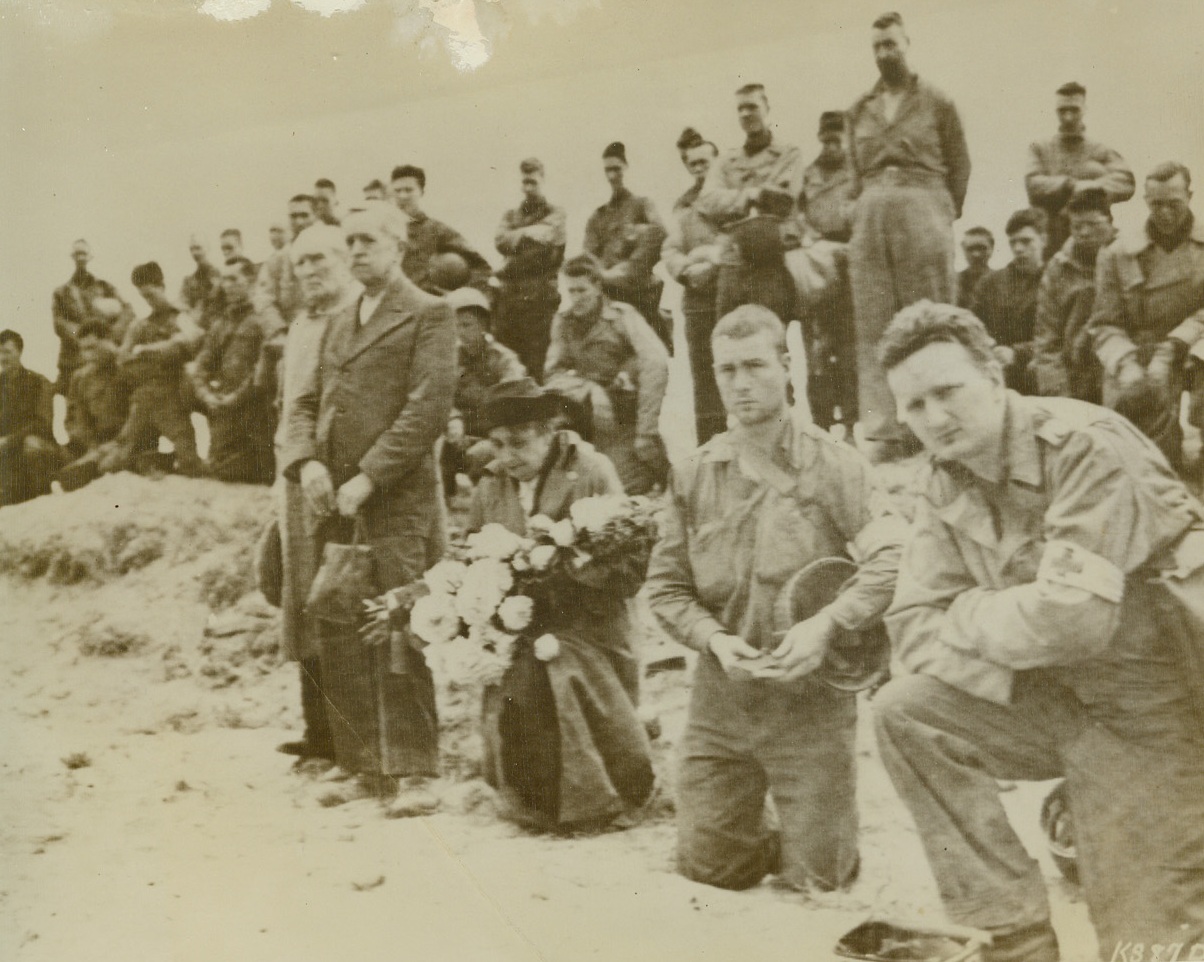 THE SUPREME SACRIFICE, 6/13/1944. FRANCE—They bring liberation to the occupied countries and protect democracy for the world, hundreds of American soldiers gave their lives in the invasion of France. A man of a liberated French town joins American troops in paying tribute to the honored dead, while his wife kneels with flowers for the graves in the first American cemetery in France. Credit (Signal Corps Radiotelephoto from ACME);