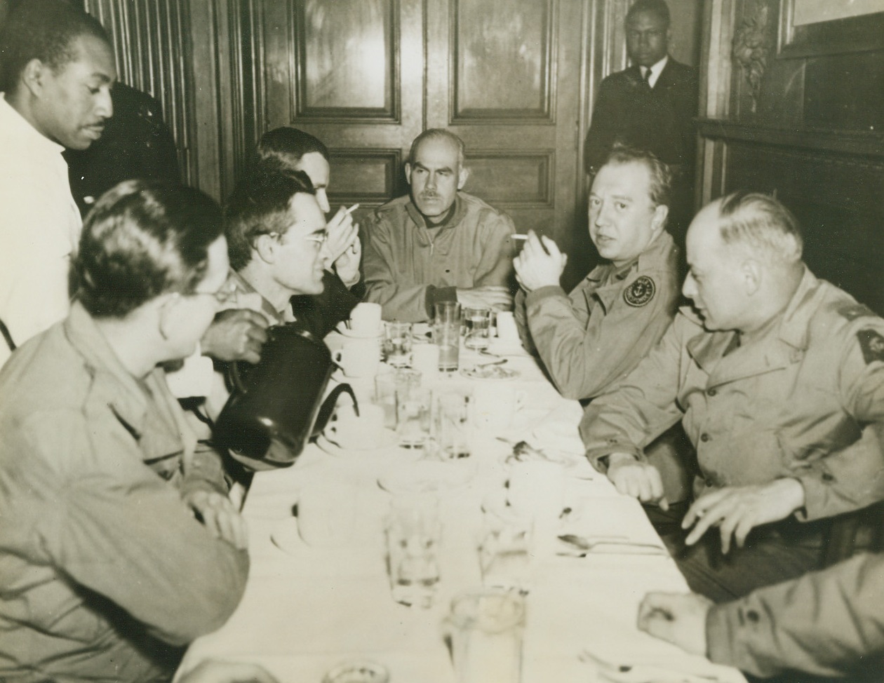 Correspondents Dig In – That’s Chow, 6/23/1944. England – War Correspondent’s who have covered the naval aspects of the invasion get together at a port somewhere in England for chow with Col. Ernest Depuis (center) of the Supreme Allied Headquarters staff. The correspondents are (left to right): Tom Wolf, of NEA; Peter Whitney, of the San Francisco Chronicle; R.L. Strout, of the Christian Science Monitor; Fred Sondern, Jr., of the Reader’s Digest; and Marcel Wallenstein, of the Kansas City Star. Credit: US Navy Photo from ACME;