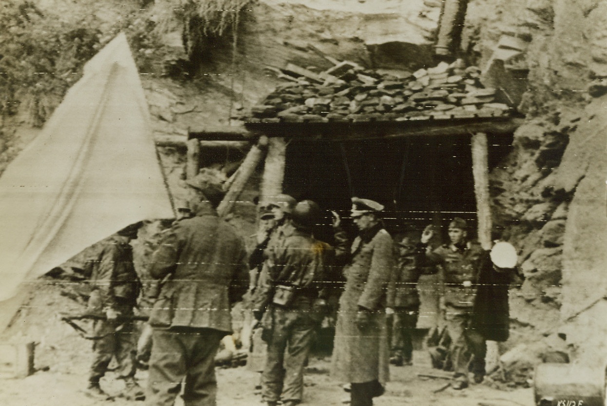 German Commanders Give Up, 6/28/1944. Cherbourg, France – A German soldier, (left, foreground) holds a white flag of truce, near the entrance to an underground fortress, as Lt. Gen. Von Schlieben, Commander of the Cherbourg Garrison, and Rear Admiral Walther Hennecke, Sea Defense Commander of Normandy, emerged with others of their command to surrender to the Americans. Credit: Army Radiotelephoto from ACME;