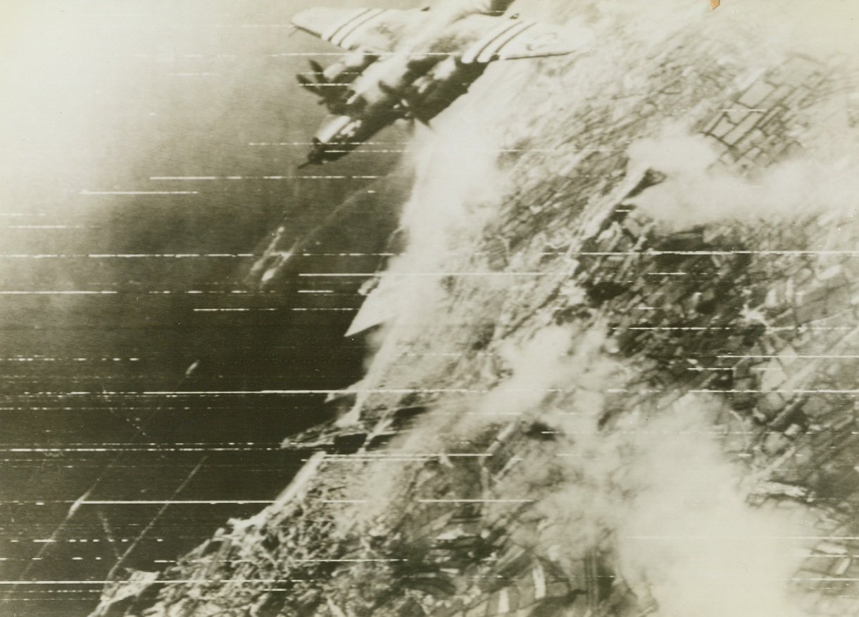 Flight Over Cherbourg, 6/23/1944. France – A Marauder Bomber from the 9th U.S. Air Force flies high over Cherbourg after loosing its message of destruction on the city. Dense clouds of smoke billow skyward from the Nazi Bastion – the result of successful bombing of German defense positions. Between 25,000 to 50,000 Nazis are trapped in the strategic port as the Allies get set to close the pincers around this important French town. Credit: Signal Corps Radiotelephoto from ACME;