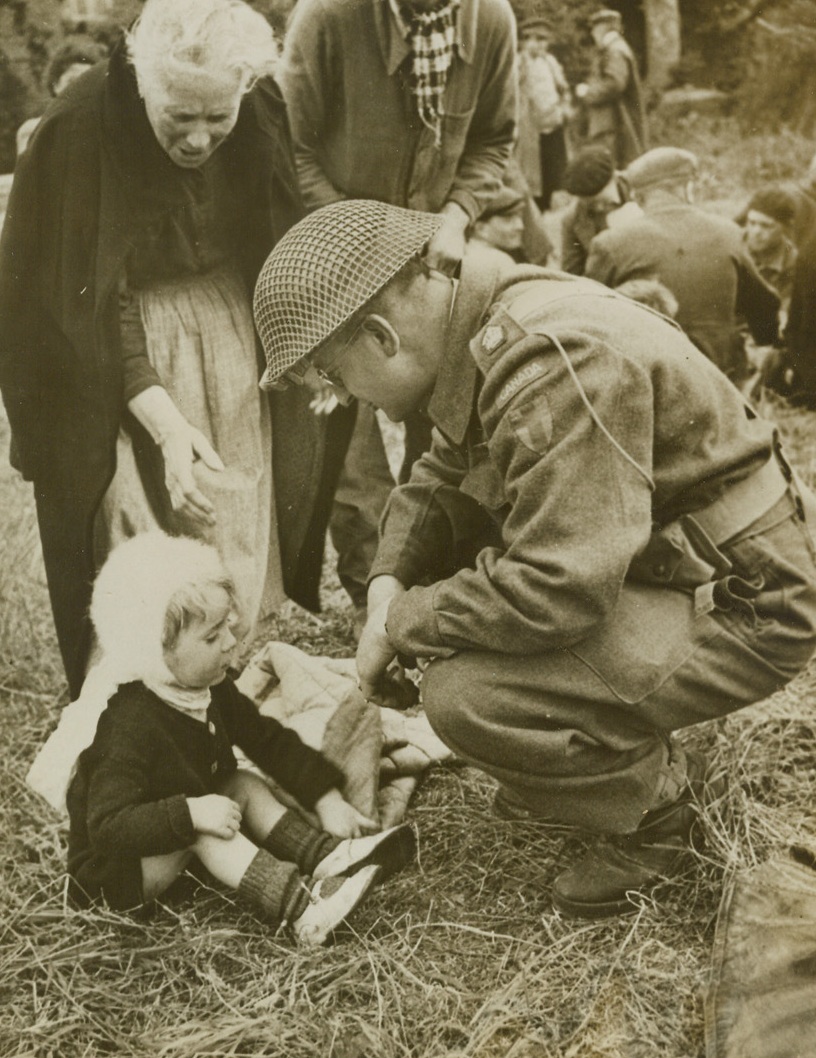 Young Frenchman Finds a Friend, 6/15/1944. Somewhere in France – A Canadian fighting man squats to chat with a young French refugee in the battle area of Normandy. The little boy and the old woman behind him were among many hungry refugees who had not eaten for three days before they were fed by the Civil Affairs Department of the Allied Forces. Credit: British official photo from ACME;