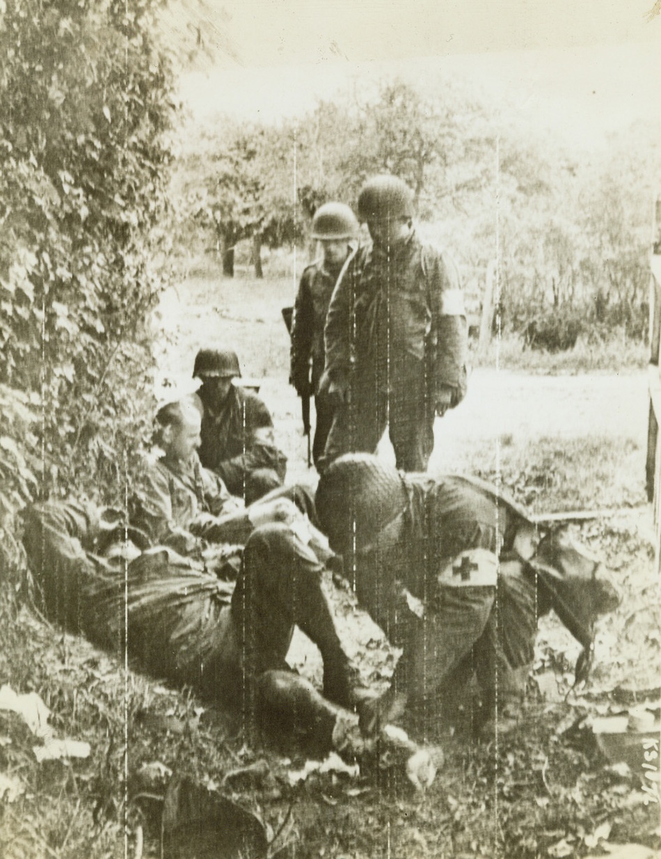 Snipers’ Victims, 6/25/1944. Cherbourg, France – Helmeted medical officers kneel to give first aid to a pair of American fighting men who were victims of snipers’ bullets on the outskirts of Cherbourg before the vital port fell to the Allies. Fighting still rages in Cherbourg although the German DNB agency says “It is to be assumed” that the key city has been captured by the Allies. Credit: Signal Corps Radiotelephoto from ACME;