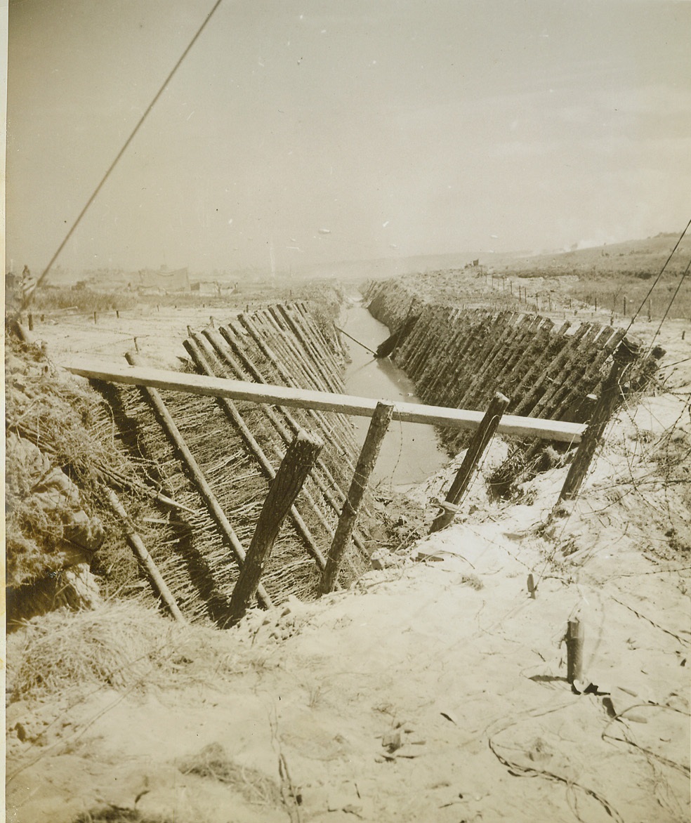 Fifteen Feet Deep and Useless, 6/19/1944. SOMEWHERE IN FRANCE -- Fifteen feet deep, reinforced with timbers, and flooded as a final precaution, this Nazi tank trap was one of the reasons why Hitler's horde thought they could sit back and take life easy -- for the Allies would never pass. But the big ditch, dug about 150 yards from the beach, failed to halt the Allied armies who were soon way past the trap and taking German strongholds inland by storm. Credit: -WP- (ACME Photo by Bert Brandt for the War Picture Pool);