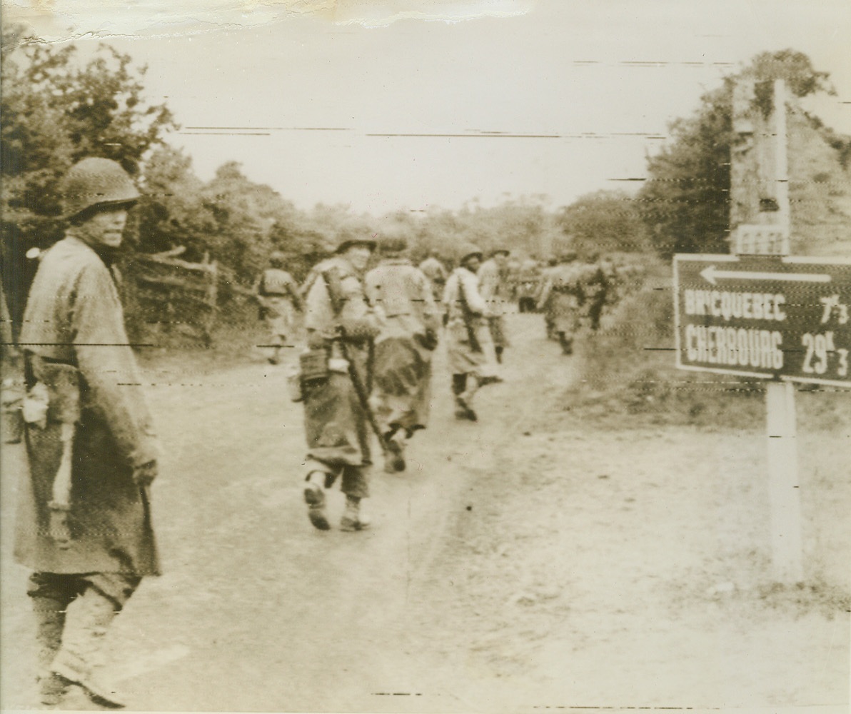 They’re Closer, Now!, 6/20/1944. France—U.S. Infantrymen head for action below Cherbourg, passing a sign giving the distance to the important city, as 29 kilometers (about 18 miles). Photo was flashed to the U.S. today, when it was announced that U.S. forces are only three and a half miles from the important channel port, and closing in fast.  Credit: Army radiotelephoto from ACME;