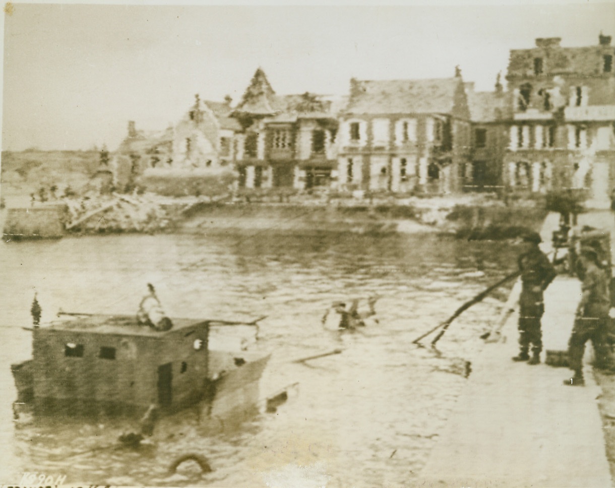 First Normandy Port Captured, 6/14/1944. France—British soldiers stand at the quayside at Port en Bessin, the first port captured by the Allies in Normandy, looking at a German flak ship which was sunk in the harbor.  Credit: British war office photo transmitted from London by Signal Corps radiotelephoto from ACME;