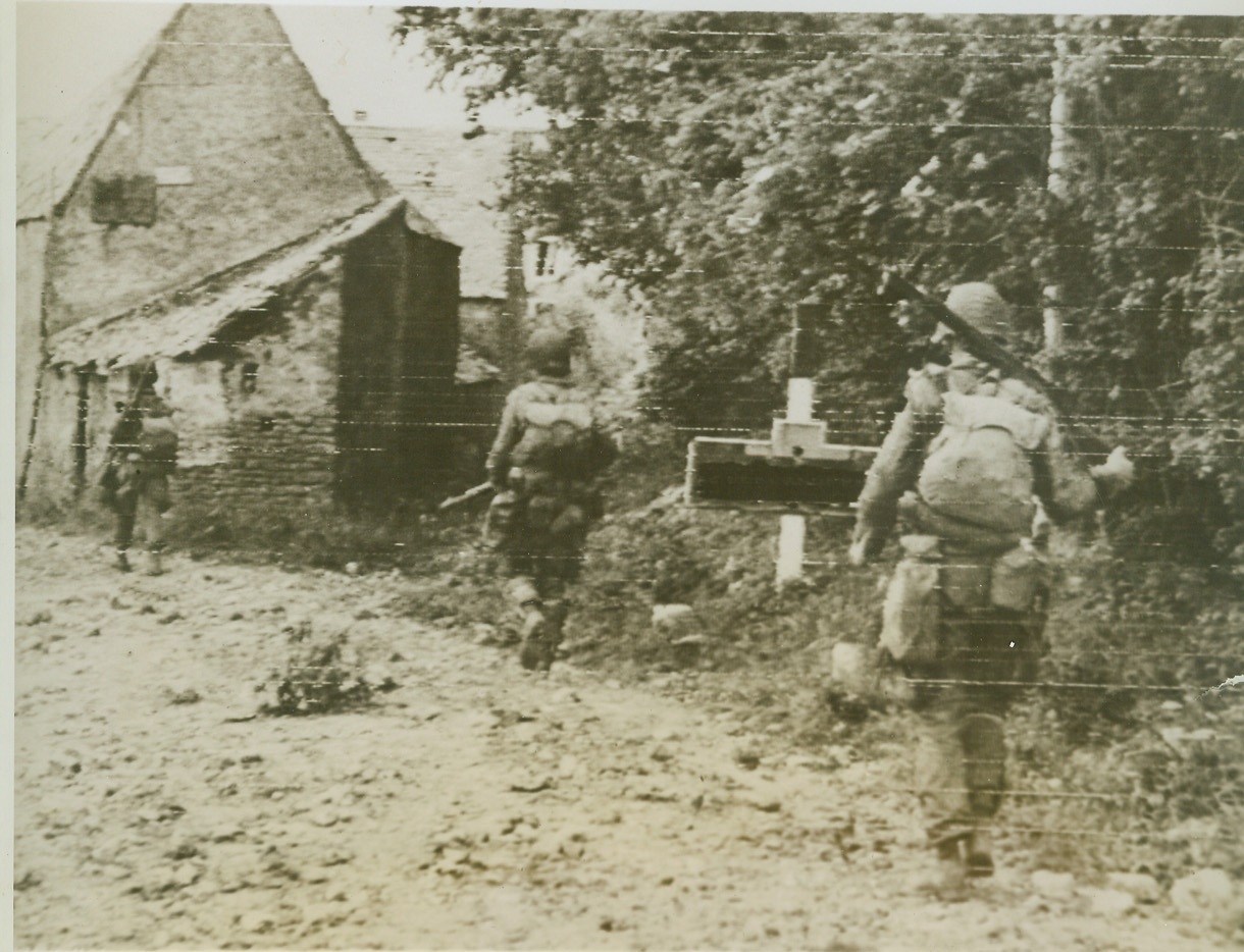 First Stop On The Road to Berlin, 6/9/1944. France—Using the countryside foliage and buildings for cover, American paratroopers move cautiously into a small village in northwestern France. Allied advances now face their first major land tests against rapidly stiffening resistance from Nazi reserves flung into the acknowledged 70-mile battleline.  Credit: Signal Corps radiotelephoto from ACME;