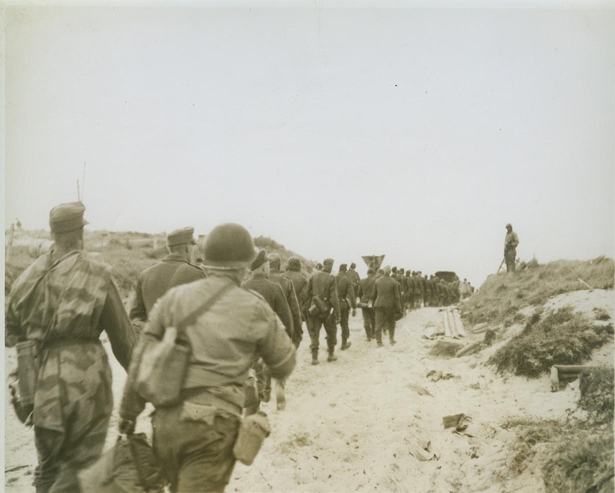 Nazis—A Motley Crew, 6/12/1944. France—Sorry about the whole thing, these German prisoners march through the sands of a Normandy beach towards the sea and transportation to England where they will be placed in prisoner of war compounds. Allied soldiers guard the column of Nazis—on the alert for any escape attempts. Credit: ACME;