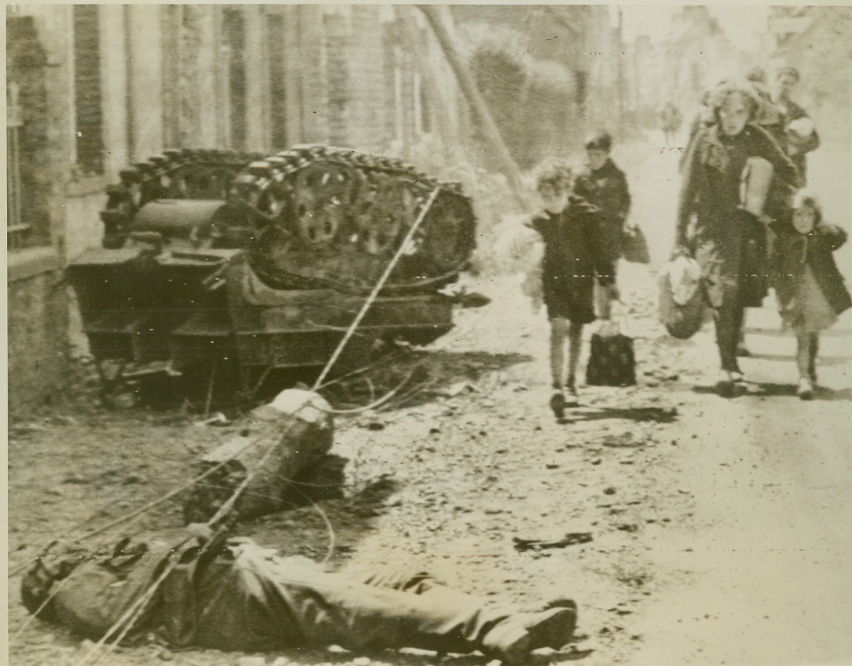 Home Is Where The Nazis Aren’t, 6/19/1944. France—Hardened by the war, a French family gives no notice to the dead German and smashed equipment as they trudge toward their home in Pont L’Abbe. In particular notice the small children who seemingly find nothing unusual in the fact that a dead Nazi lies in the street. Pont L’Abbe was one of the last towns taken by the Allies before isolating the Port of Cherbourg.  Credit: Signal Corps radiotelephoto from ACME;