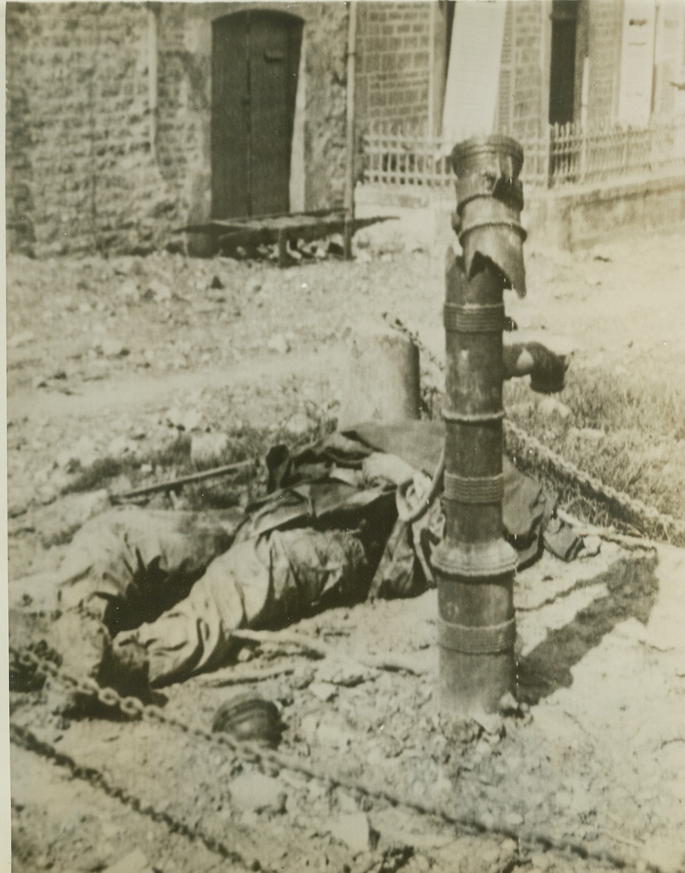 Victim of Nazi Trick, 6/18/1944. France—Treacherous Germans planted a booby trap in the water pump of a small German village on the Cherbourg peninsula—a trick that spelled death for this unsuspecting Yank. The ill-fated American lies beside the wreckage of the pump at which he met violent death. Credit: ACME photo via Signal Corps radiotelephoto;