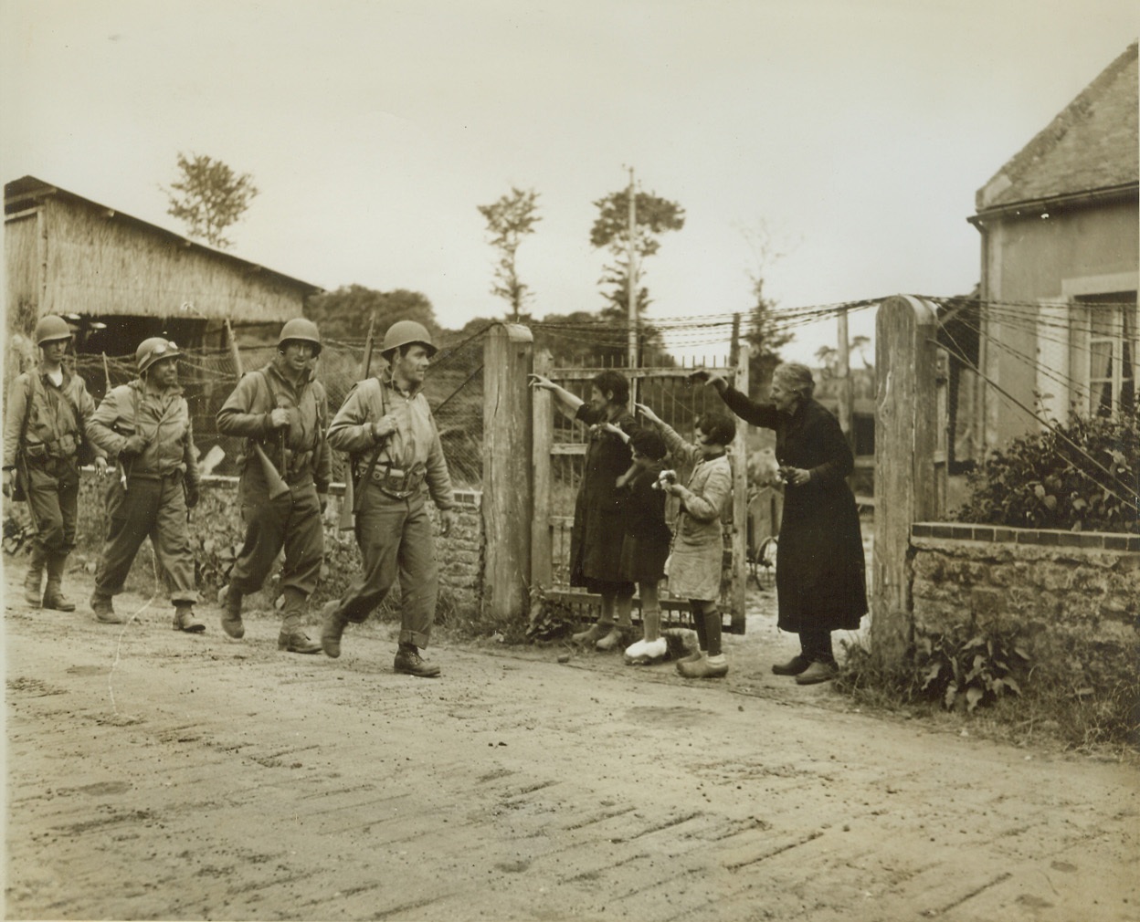 Liberators Are Welcome, 6/13/1944. France—Four female members of a French family stand by the gate of their modest farmhouse to offer a cheerful welcome to American infantrymen passing through the liberated village. The two little girls hold gifts of flowers for the liberators. Credit: ACME photo by Bert Brandt for war pool correspondents;