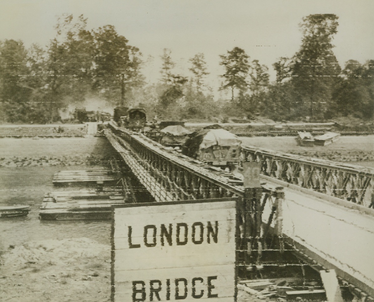 “LONDON BRIDGE” TO BERLIN, 7/20/1944. FRANCE—In the wake of the terrific tank battle that forced a break through north of Caen, British troops cross “London Bridge” set up across the Caen canal. Quickly assembled, the bridge is a Bailey Bridge and is strong enough to hold the truck loads of supplies needed by battling forces. Credit: British War Office photo via Signal Corps radiotelephoto from Acme;