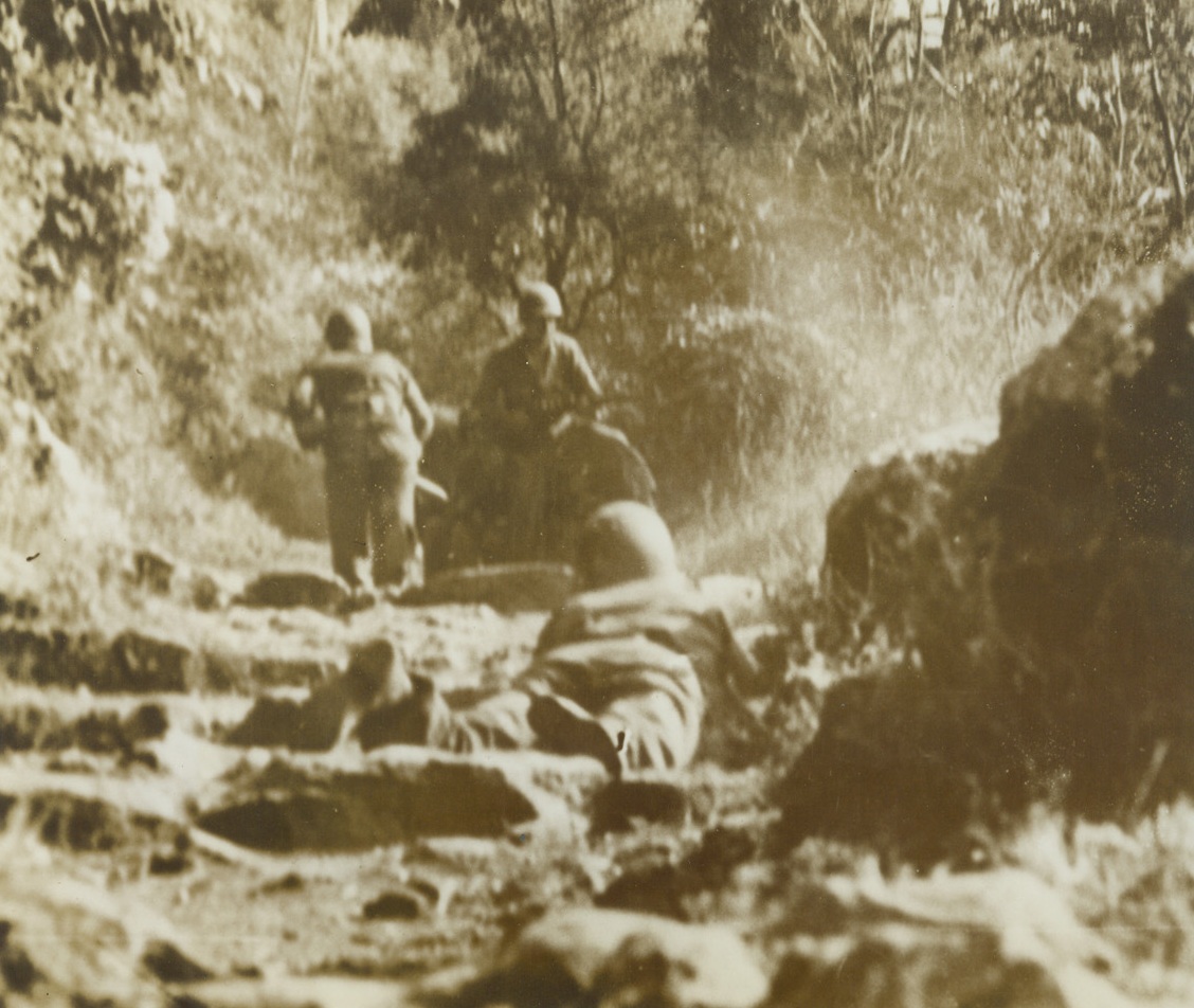 Yanks in a Spot – 1, 7/14/1944. Nemi Valley, Italy – Once the peaceful site of fragrant vineyards and the center of a flourishing wine-grape business, beautiful Nemi Valley, near Rome, was turned into a hot spot recently when a scouting patrol of Yank Infantrymen, guided by Italian Partisans found German strength much greater than they had suspected. Our boys had to fight their way out through holes in a wall of enemy machine gun fire. Here, one member of the patrol has completed his dash across the hot spot while another Yank lies on the ground, waiting his turn to run for it. Credit: Yank Magazine photo from ACME;