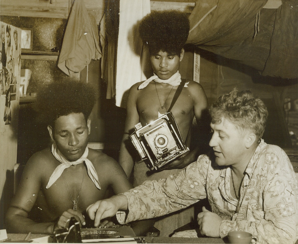 ACME Photo Turned New Guinea Prof., 7/14/1944. Port Moresby, New Guinea – ACME Newspictures War Correspondent, Frank Prist, Jr. seems to be in fairly good shape for secretaries at his office in Port Moresby, New Guinea. To make sure that his native help know the workings of American machines he is well prepared, and qualified, to turn professor of typewriterology. As he teaches one of the boys where to punch the dollar sign on the keyboard, the other turns the tables on Prist and becomes cameraman for the occasion. By the way, that’s Prist on the extreme right.Credit: ACME photo by Frank Prist, Jr., War Pool Correspondent.;