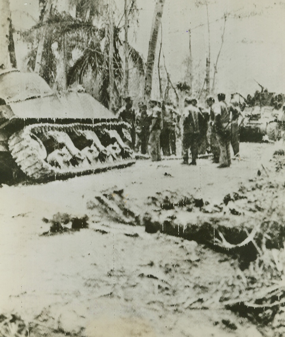 First Photo of Yank Troops in Guam, 7/29/1944. Guam – In this first photo to arrive here from the new fighting front on Guam, a group of Marines bunch together while clearing a tank trap on a road after one of their tanks was temporarily put out of action. Yanks are hot in pursuit of Japs occupying this first of American Pacific possessions to fall into enemy hands.Credit: Signal Corps Radiotelephoto from ACME;