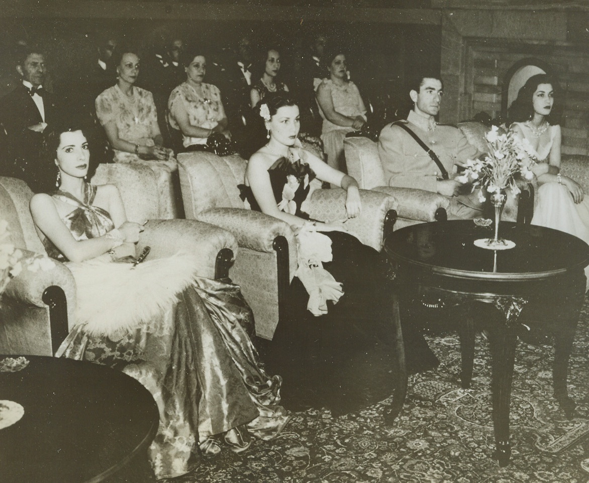 U.S. Stars Give Concert for Royalty, 7/27/1944. Iran – While in the Persian Gulf Command giving concerts for the troops, Andre Kostelanetz, Lily Pons, and other American artists also gave a performance for Iranian Royalty. Here, listening to the performance, are (in first row): Princess Ashraf Pahlevi, sister of the Shah; Her Imperial Majesty, the Empress of Iran; His Imperial Majesty, Mohamed Reza Pahlevi, Shahinshah of Iran; and Princess Shams Pahlevi, another sister of the Shah, recently married to a doctor or Egyptian Nobility. (Passed by Censors)Credit: ACME;
