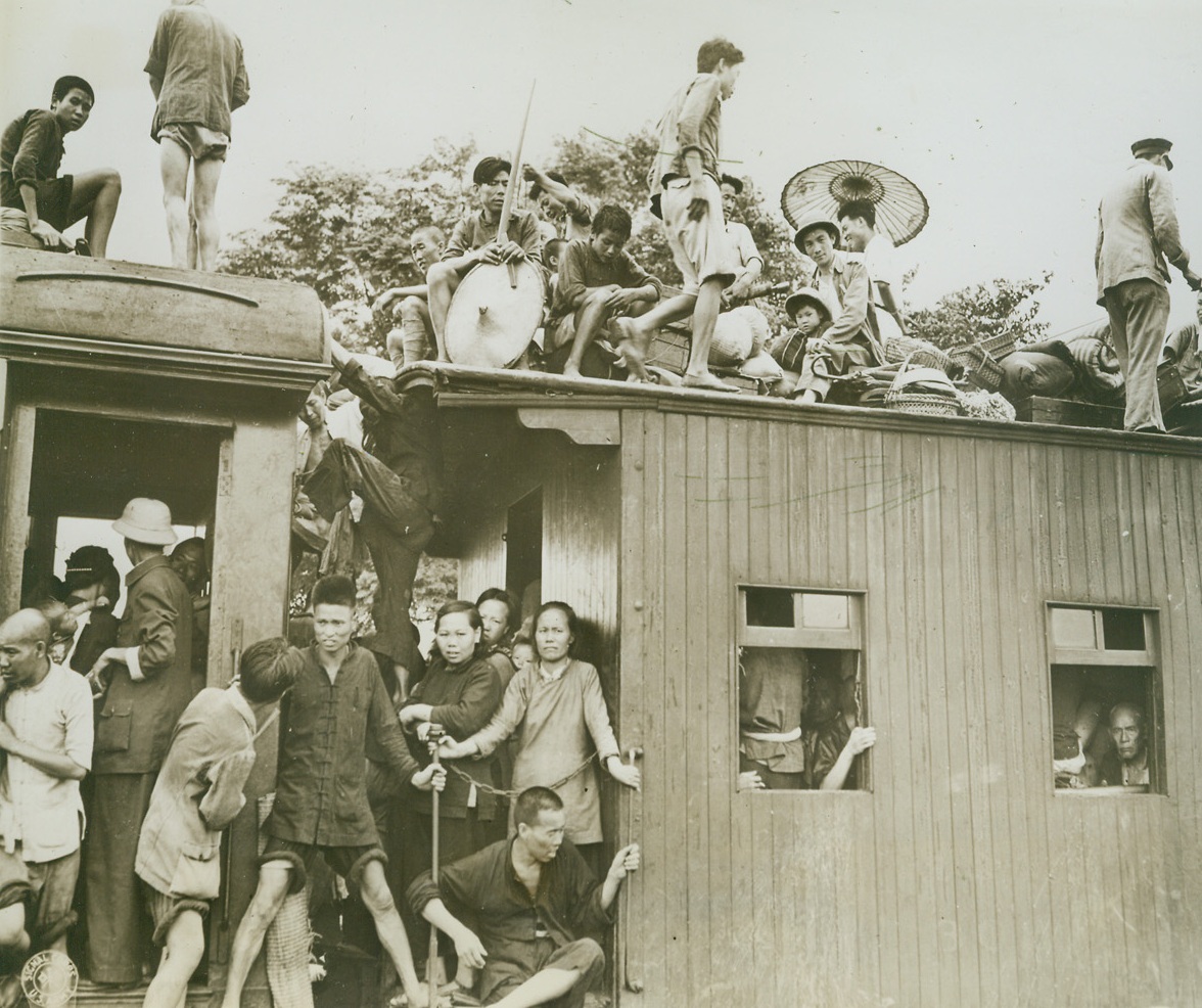 No Pullman Accommodations Here!, 7/20/1944. Chinese evacuees occupy every available inch of space on this train as it leaves South station in Kweilin, China, when Jap forces threatened the city last June.  Some of the passengers are perched in dangerous spots between cars, others have belongings piled on the roof.  Note one Chinese with parasol.  This photo was released in Washington Today.Credit Line (U.S. Army photo from ACME);