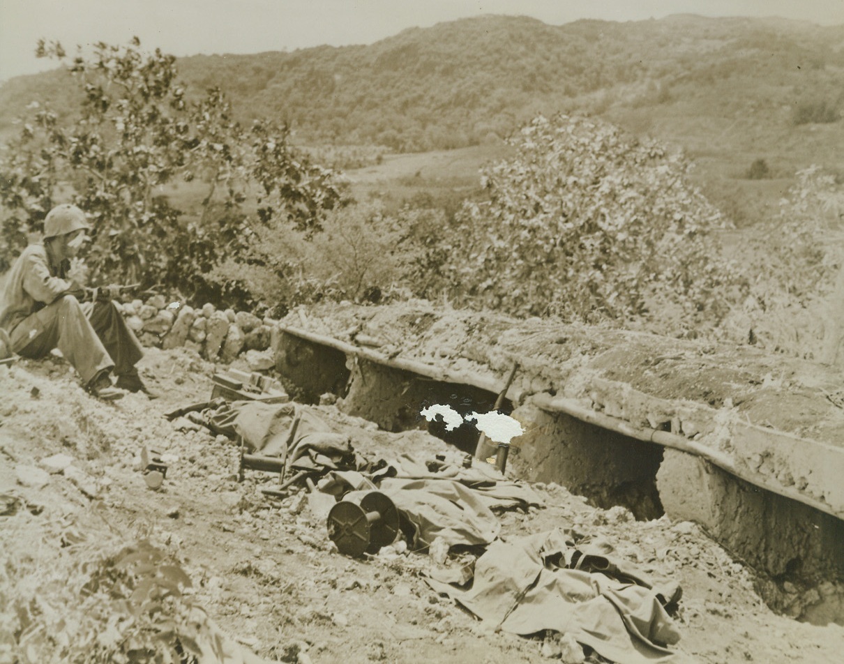 LONE VIGIL, 7/8/1944. SAIPAN, MARIANAS —A wounded marine keeps a lonely vigil over the poncho-covered forms of dead comrades as he awaits evacuation to a rear base on Saipan. Soldiers were killed and their guardian wounded while cleaning out the Jap pill boxes at right. Total dead on Saipan has exceeded by three times the number killed in the battle of Tarawa. Credit: MARINE CORPS PHOTO FROM ACME.;