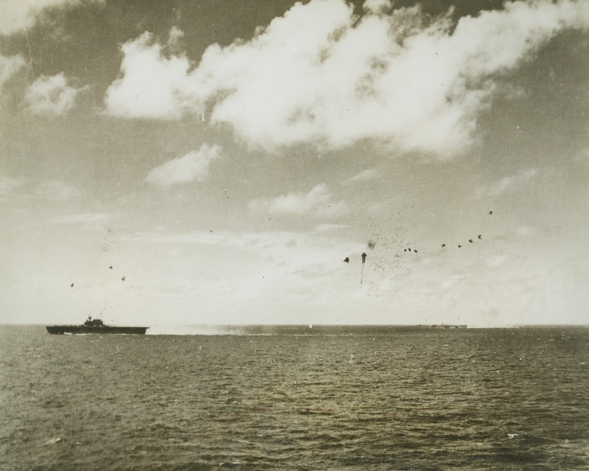 JUST A WRECK OF ITS FORMER SELF, 7/8/1944. SAIPAN, MARIANAS—A Jap dive bomber (right) is shot into tiny pieces as it moves in to attack the U.S. carrier during the big air battle off Saipan, when Adm. Mitscher’s fleet engaged the Jap navy. No lives were lost in this air battle, but two pilots were killed in a night crash on deck. American forces invading Saipan have shoved the Japs into a small six square mile space on the Island. Credit: ACME.;