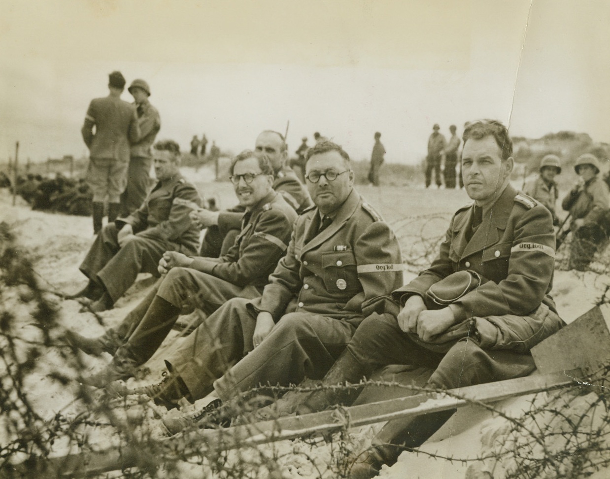 They Built the Impregnable Wall, 7/3/1944. NORMANDY, FRANCE - From behind their barbed wire cage, these officers of the German ...Organization Labor Battallion watch with interest (and is there a trace of disdain?) the Yanks who were partially responsible for the downfall of the Atlantic Wall and the Siegfried Line which the...Organization built. Taken prisoner when the allies invaded the French Coast and blasted the famed wall into nothingness, these master minds of engineering will go into hibernation for the duration.;