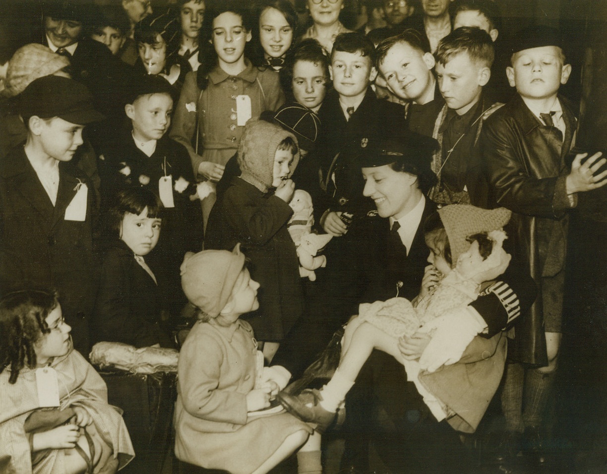 Children Evacuated from London, 7/14/1944. London, Eng.—A policewoman reassures these children who are being evacuated from London to a zone which is safe from the Nazi flying bombs which have been hitting at southern England. Tagged for identification, these youngsters embark upon their new adventure with smiles, even though most of them are leaving their parents behind in London. Credit: ACME;