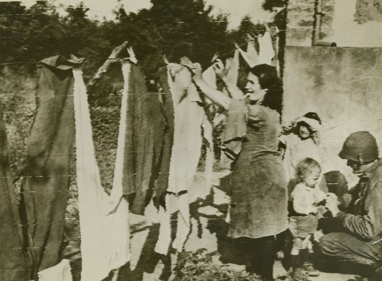 Frenchwoman Does G.I. Laundry, 7/18/1944. St. Lo, France—A happy G.I., relieved of his wash day duties, entertains some French youngsters while their mother hangs some G.I. laundry on the line. The soldier is T/Sgt. Olin Dows, Rhinebeck, N.Y.  Credit: U.S. Army radiotelephoto from ACME.;