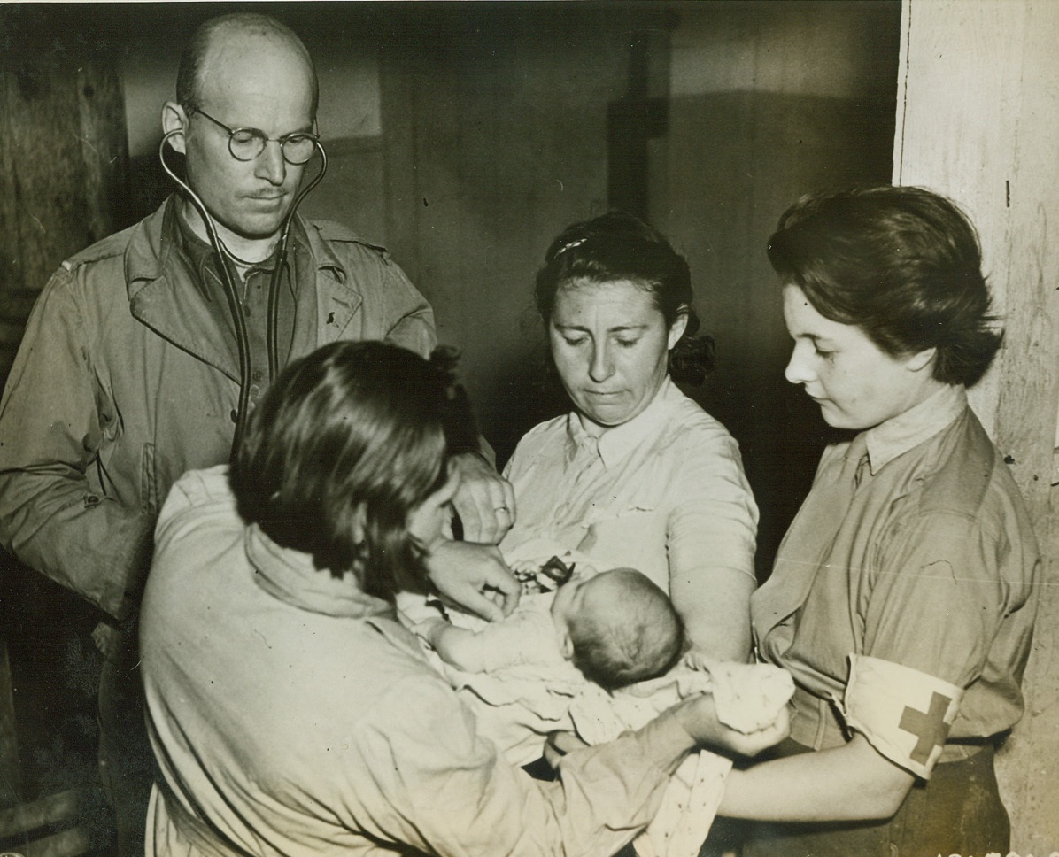 MEDICAL AID FOR FRENCH BABY, 7/25/1944. FONTENAY-SUR-MER, FRANCE – Lt. Samuel J. Ravitch, of Quincy, Fla., U.S. Army medical officer with a civil affairs unit, examines a French baby.  Helping him, are (facing camera): Eugenia Fuchs (center), former surgeon with the Russian forces at Leningrad, who was captured by the Germans and forced to care for TODT organization workers; and Louise Portman, a Swiss girl, member of the medical corps of the Free French Army.Credit: U.S. Army photo from Acme;