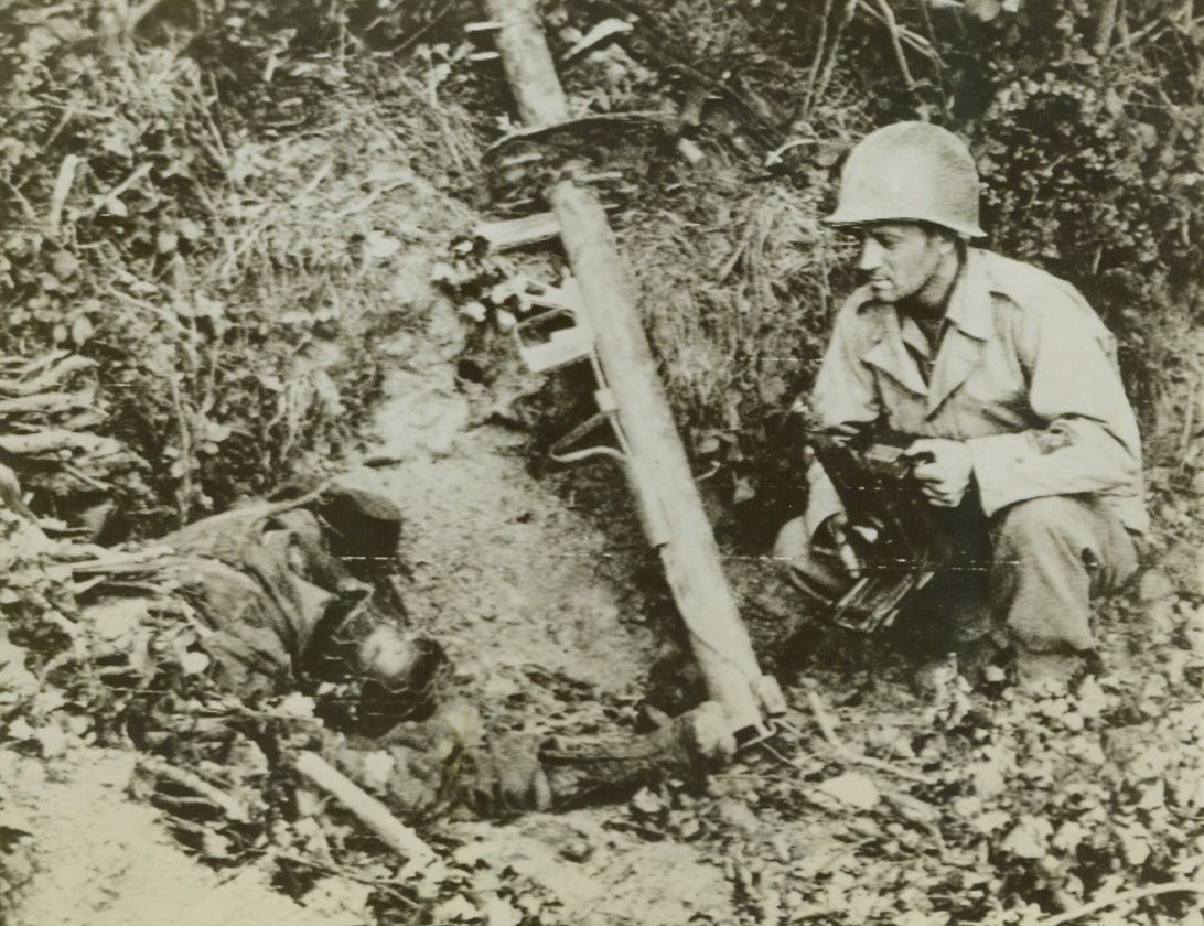 Title Covered, 7/29/1944. FRANCE—Sprawled by his weapon, a Nazi bazooka gunner lies dead, a victim of the terrific allied aerial and artillery attack in the Marigny area of France. A U.S. Signal Corps photographer, camera in hand, looks over the gunner and the weapon which will no longer toss shells at American tanks. Credit (Signal Corps Radiotelephoto from ACME);