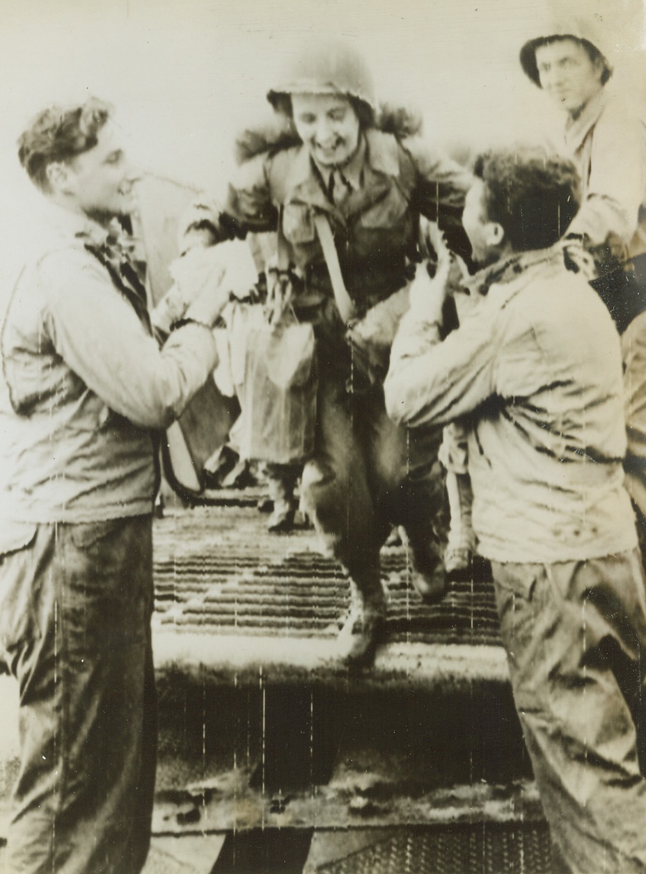 WACS ARRIVE IN FRANCE, 7/18/1944. FRANCE—Grinning G.I.’s willingly assist some of the first US WACS to land in France. Note the soldier on the left still clutching mail in his hand. Credit (US Army Radiotelephoto from ACME);