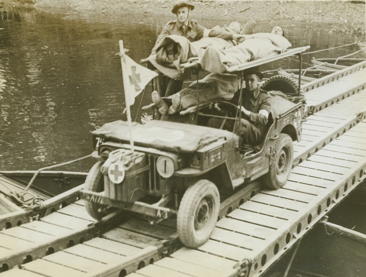 Wounded Tommies Ride Double Decker, 7/7/1944. France – Wounded in the fierce assault that stormed the River Orne and enabled the British to take Caen, three Tommies ride a Double Decker Jeep, manned by two medics, on their way to the rear for treatment. Note the hastily constructed pontoon bridge stretched across a stream. Credit: ACME;