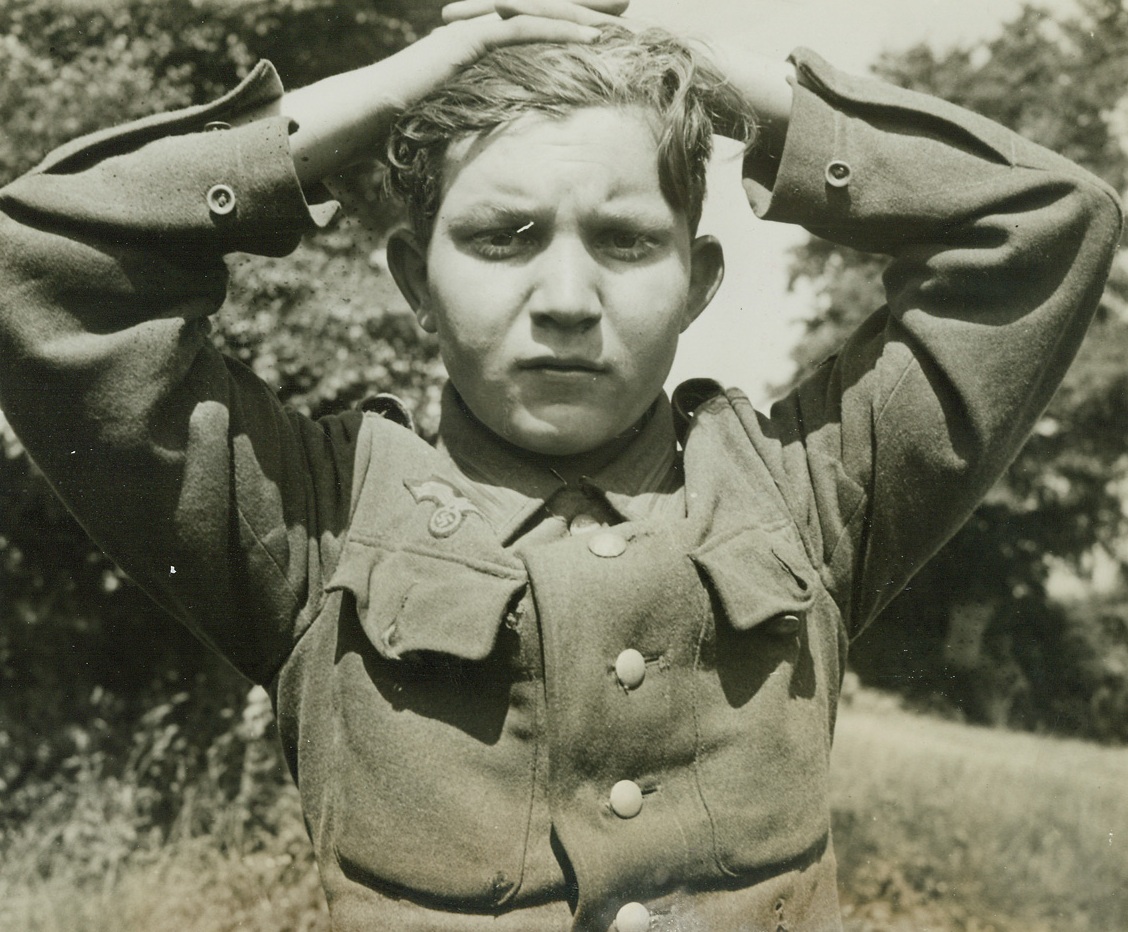 Nazi Youngster Plays Soldier, 7/1/1944. France – Hands over his head, this youthful Nazi was among the thousands captured by victorious Allies in Cherbourg. Only 16 years old, his boyish face belies the fact that the Nazis have made him a killer capable of brutalities of the oldest and most ruthless followers of Hitler. To get children like this back to schools and off the battlefields is one of the reasons—part of the cause the Allies are fighting for. Credit: ACME photo by Andrew Lopez, War Pool Correspondent;