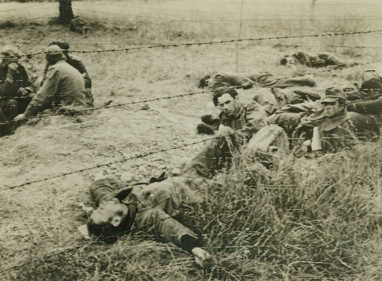 Exhausted Captives, 7/17/1944. St. Lo, France – Battle weary and dazed after witnessing the intense artillery fire from Allied big guns in the St. Lo sector, these German prisoners lounge in a prisoner of war enclosure behind the fighting lines. Lying flat on his back, arms flung out, the captive in foreground sleeps the sleep of exhaustion. Credit: Signal Corps photo from ACME;