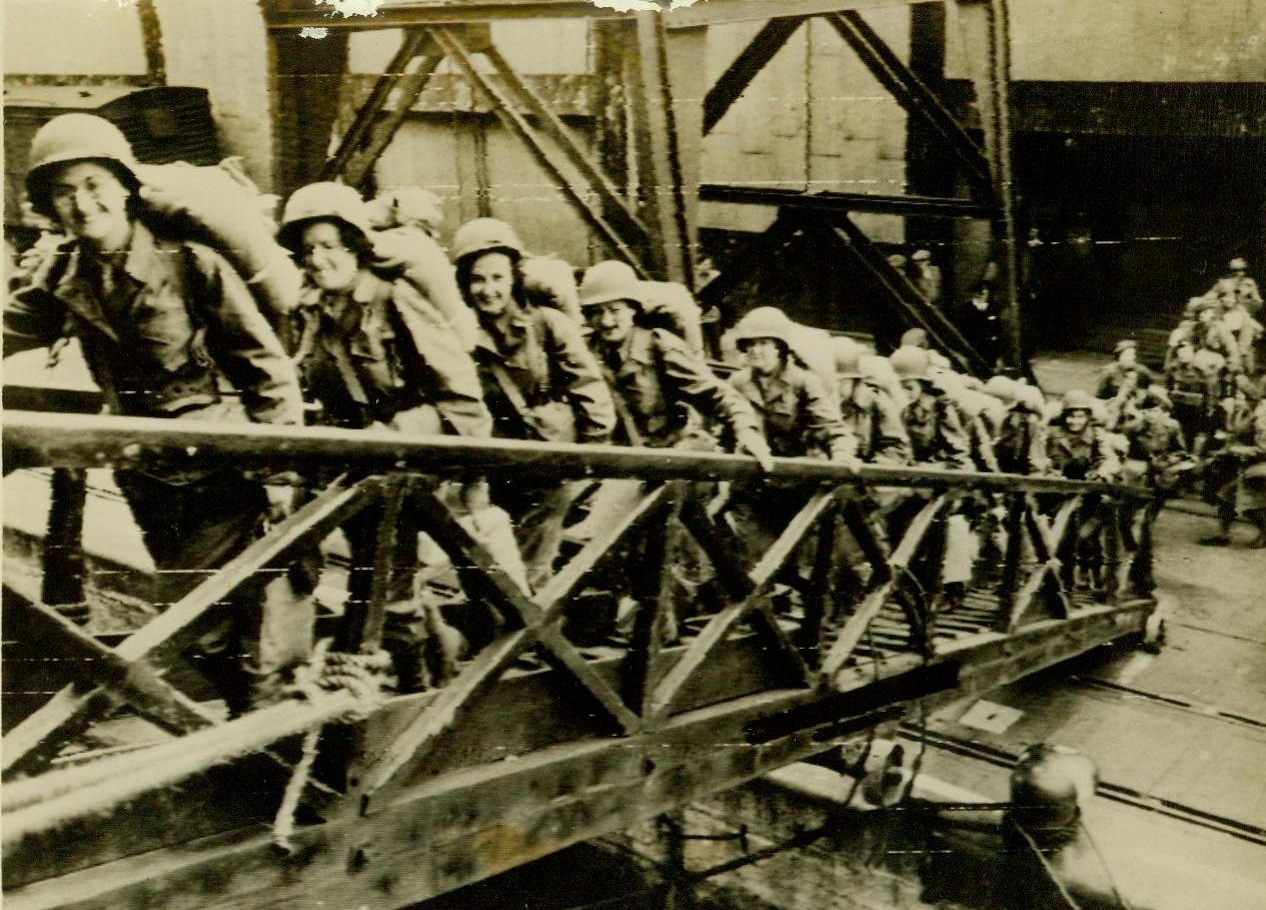 First To Go Over, 7/17/1944. First To Go Over England—The first group of WACs to be sent to France to serve with allied forces, these American women flash happy smiles as the climb up the gangplank of their transport mighty happy about their trip “over there” The girls embarked from a port somewhere in England 7/17/44 (Radiotelephoto—ACME);