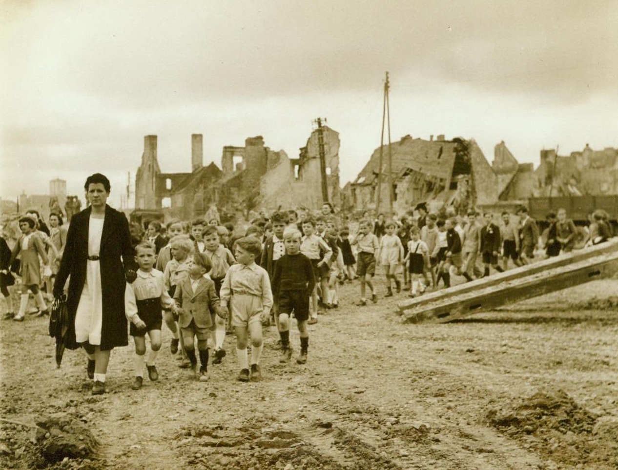 Head For Bastille Day Festivities, 7/19/1944. France -- Marching in orderly fashion past the ruins of their homes, French children head for Bastille Day celebrations in the town of Isigny. Festivities took the form of services at the war memorial in the little Normandy town. 7/19/44;