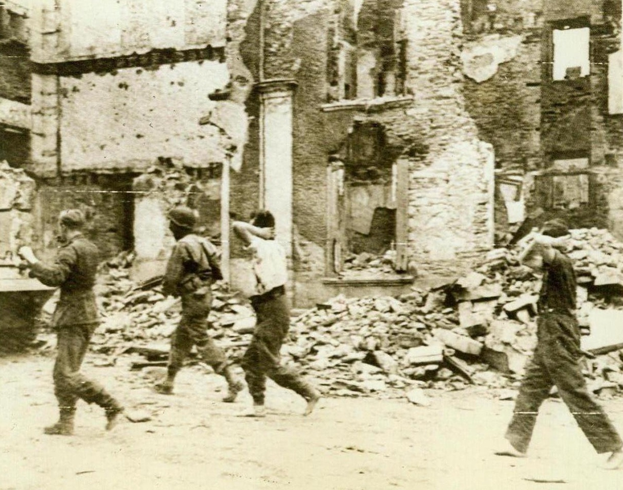 Germans Captured In St. Lo, 7/20/1944. France -- An American Soldier (Second from left, background), herds three Germans through a rubble-strewn street in St. Lo. The prisoners have their hands over their heads and the two at the right are barefooted. Photo as taken as Yanks wrested the town from the enemy. 7/20/44 (ACME);