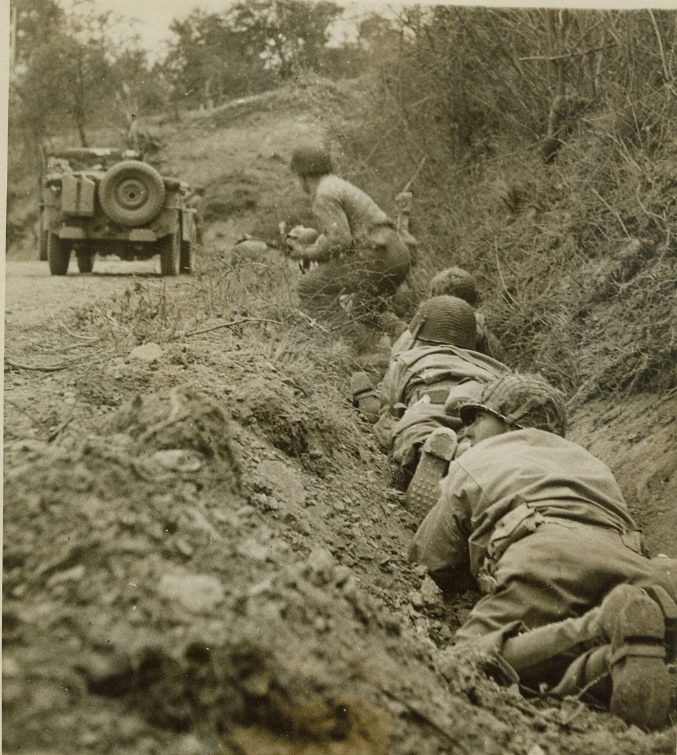Creeping Up, 7/24/1944. St. Lo, France—In the vicinity of St. Lo, American soldiers inch forward in their foxhole along the side of a road, while they dodge German mortar and machine gun fire. After an eight-day fight, Yank troops captured the town.  Credit: ACME photo by Andrew Lopez, war pool correspondent;