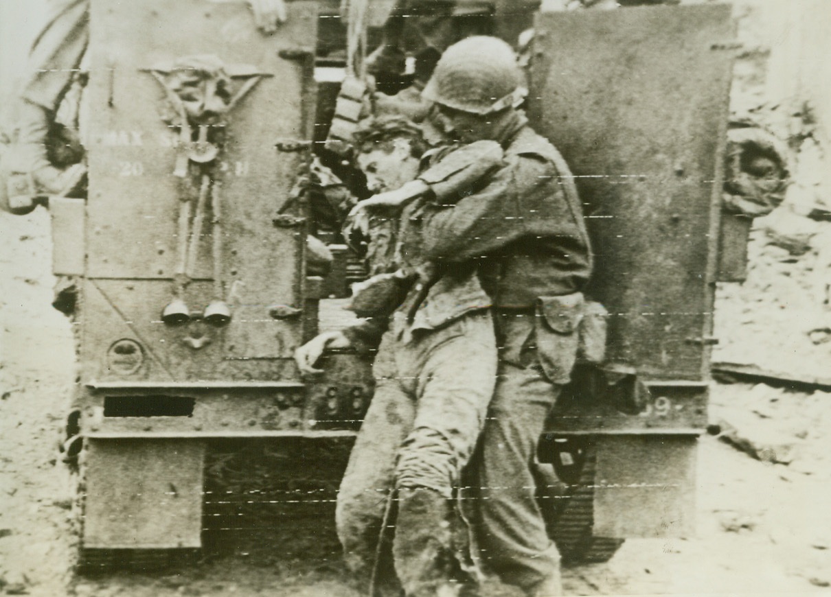 Wounded Nazi Rescued By Yank, 7/22/1944. St. Lo, France—An American soldier picks up a wounded Nazi on the road to St. Lo and puts him in a halftrack after he was abandoned by his comrades.  Credit: U.S. Army radiotelephoto by ACME;