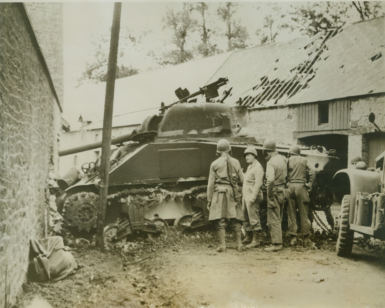 Allies Finally Get Foothold on La Haye, 7/9/1944. La Haye Du Puits, France—American soldiers look over one of their medium tanks, blocking a passage in La Haye Du Puits after it had been knocked out by German guns. The American forces, after being in and out of La Haye for five days, finally held it yesterday (July 8) against fierce German resistance. Although our forces have officially captured the city, German snipers continue to rain bullets into the streets.  Credit: ACME;
