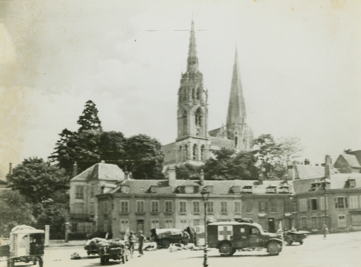 YANK MEDICS AT WORK IN CHARTRES, 8/22/1944. FRANCE - - Working in the shadow, of the famous 12th century Cathedral in Chartres, Yank medics give aid to wounded before continuing the push Eastward toward and beyond the Seine. Credit: Army Radio telephoto from Acme;