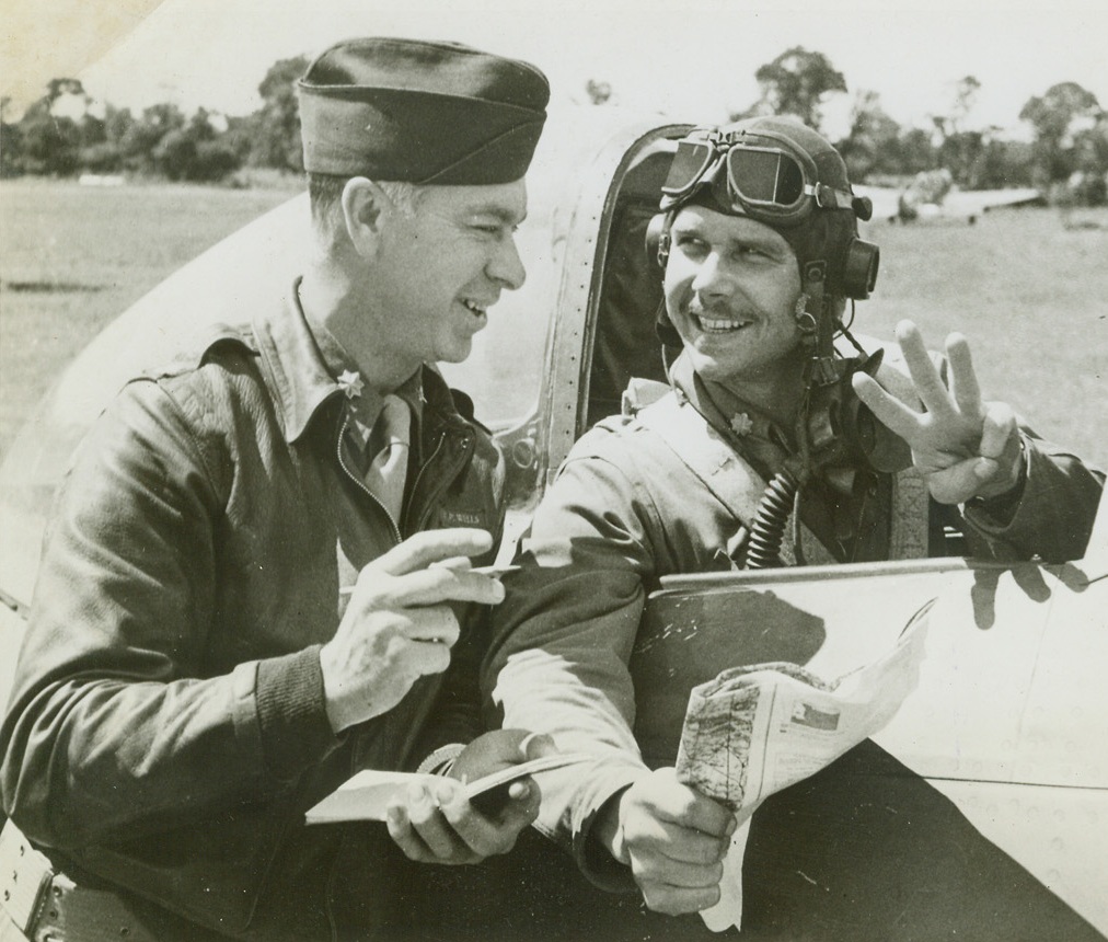 Three Planes, Sir, 8/8/1944. France – Returning from a mission in Normandy, Maj. Rockford V. Gray, Dallas, Texas, reports to Intelligence Officer Maj. Perry Wells, Chicago, Illinois, his quota of three German planes downed during the flight over British lines. These three brought Maj. Gray’s score of planes downed to seven. He has flown 102 combat missions and 182 sorties. Credit: ACME;