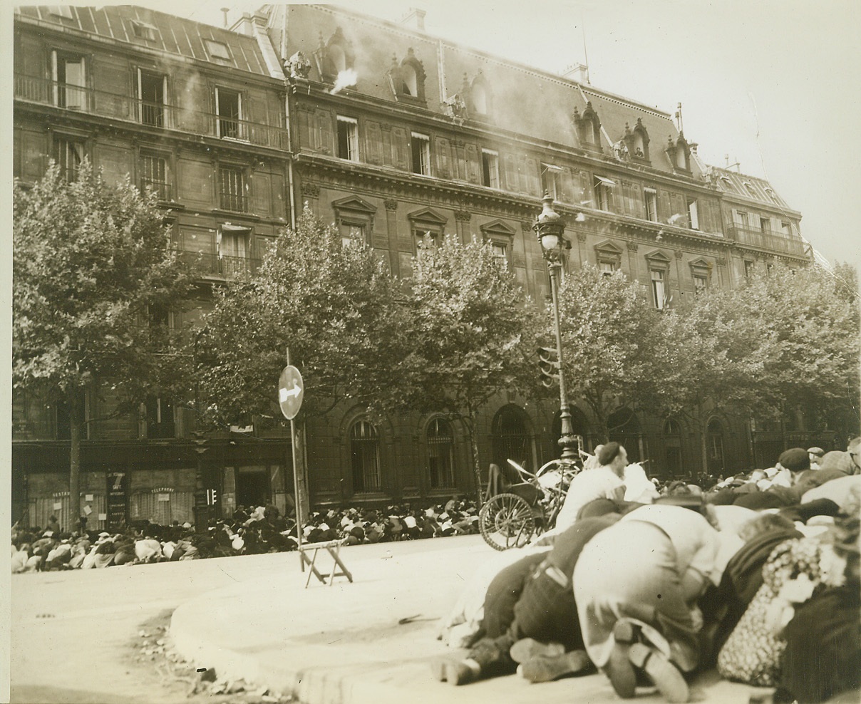 Bullets -- Unwelcome Guest at Celebration, 8/30/1944. FRANCE -- Part of the huge crowd gathered to pay tribute to Gen. Charles De Gaulle as he entered liberated Paris, crouch for cover as enemy sniper fire breaks up the celebration. Note the gun flash from the top floor, center, of the building at left and the smoke from gunfire still lingering in the air. Credit -WP-(ACME Photo by Andrew Lopez, War Pool Correspondent);