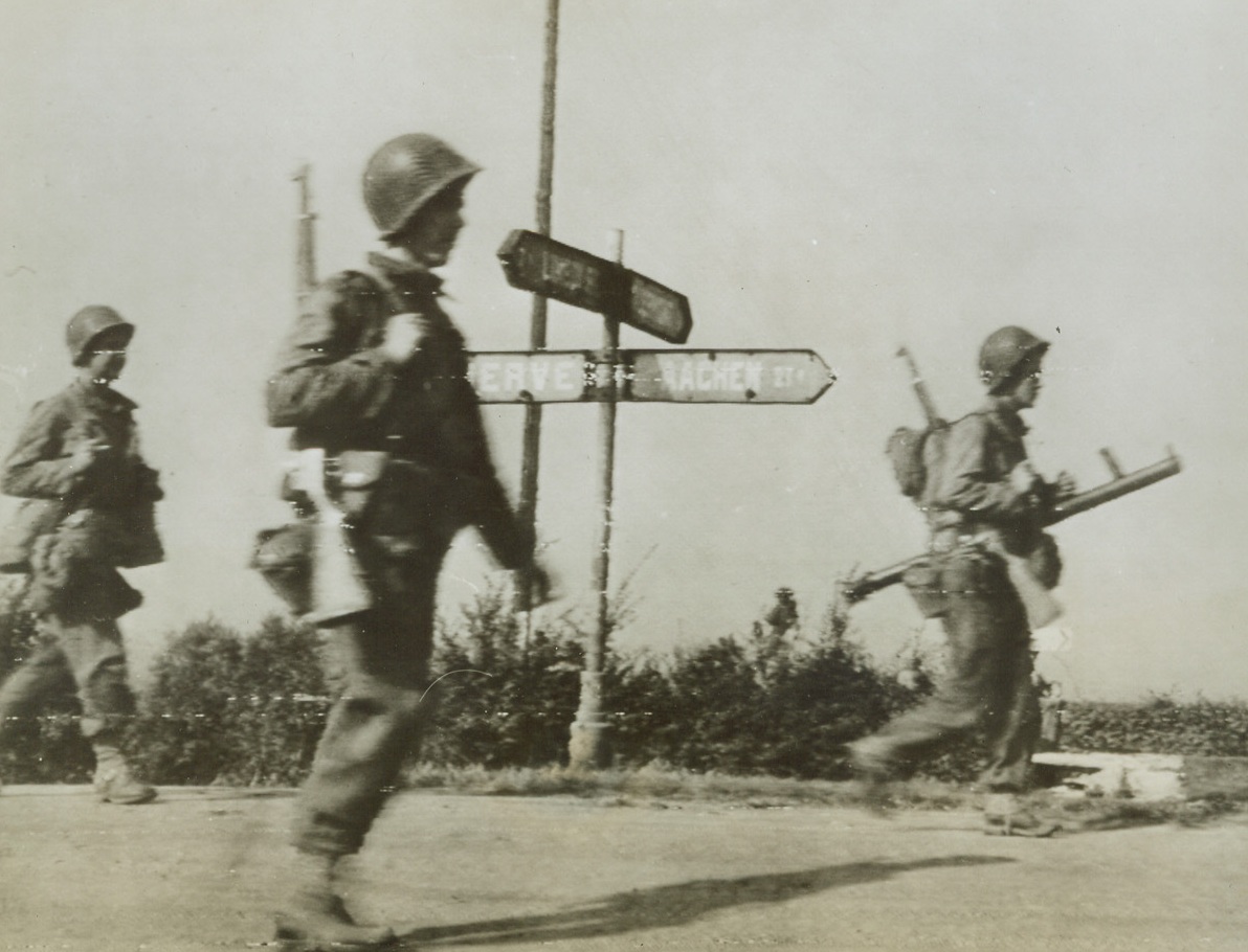 Heading for Aachen, 9/16/1944. GERMANY—Three American soldiers, one toting a bazooka, march briskly along a highway toward the key German city of Aachen. German civilians in the Aachen area have been ordered by Nazi leaders to evacuate their homes and meet the advance of American troops with “fanatical resistance.” Credit: ARMY RADIOTELEPHOTO FROM ACME.;