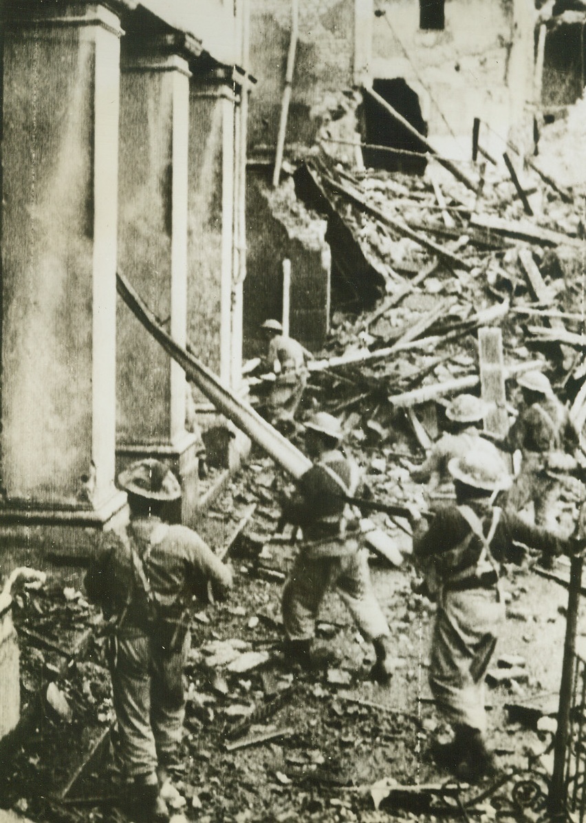 RIMINI MOPUP, 9/29/1944. RIMINI—Stepping over piles of debris in captured Rimini, Greek infantrymen “mop up” the Adriatic port. Credit: British official photo via Army radiotelephoto from Acme;