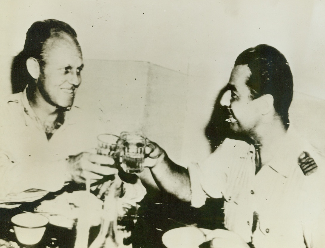 TOAST TO THE HOAX, 9/3/1944. ITALY—Lt. Col. James A. Gunn, San Antonio, Tex., (left) drinks a toast with Capt. Bazu Cantaguzino at a 15th AAF base in Italy. The Romanian pilot flew Col. Gunn back to Italy in a stolen ME-109 to arrange for the mass evacuation of over 1,000 former air forces combat crew members from Romanian prison camps. Credit: Signal Corps radiotelephoto from Acme;