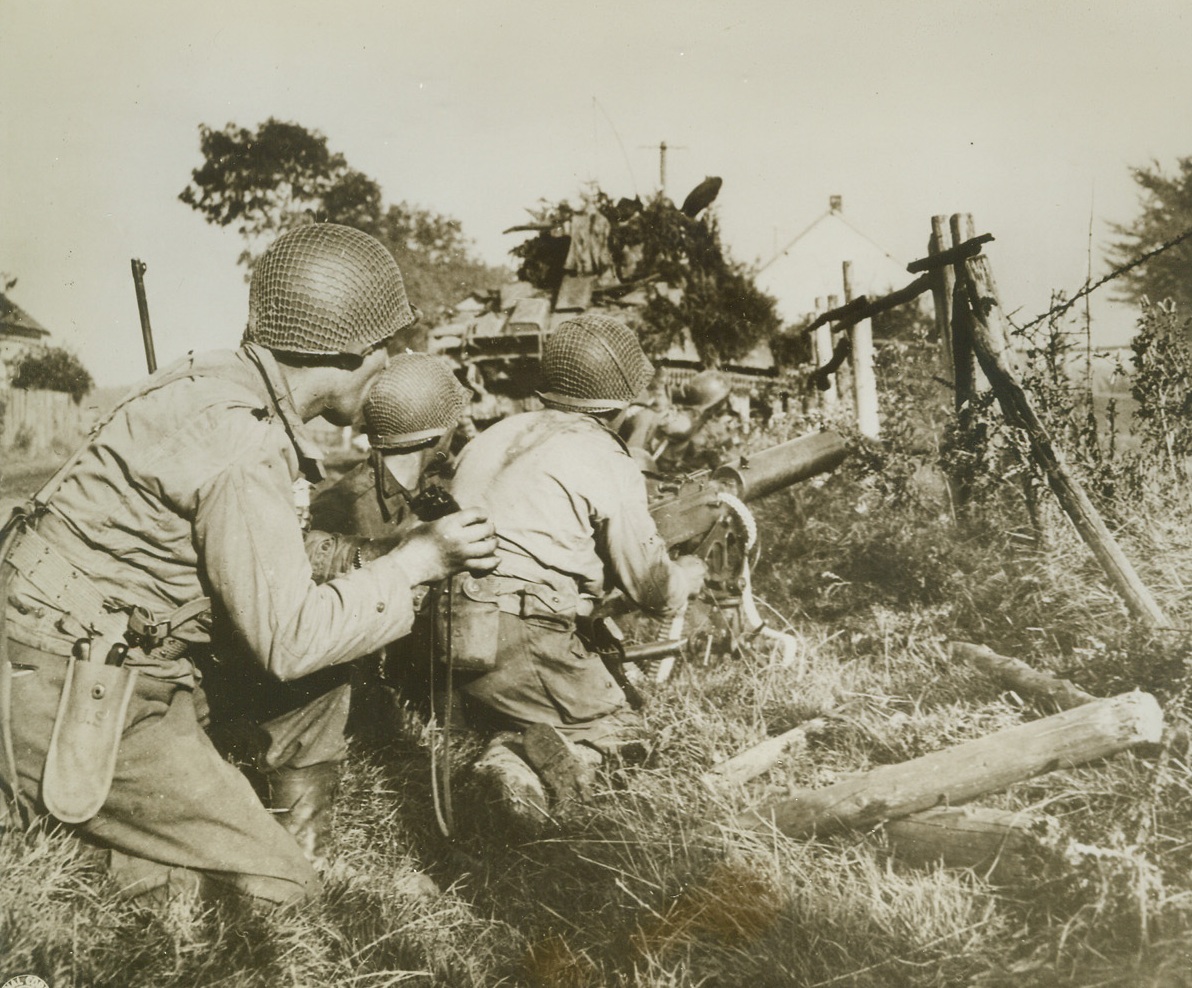 Blast Away at Enemy Positions, 9/22/1944. ROTH, GERMANY -- American machine gun crew crouches tensely by a roadside in Roth, Germany, as a camouflaged tank opens up on Nazi positions. Credit (Signal Corps Photo from ACME);