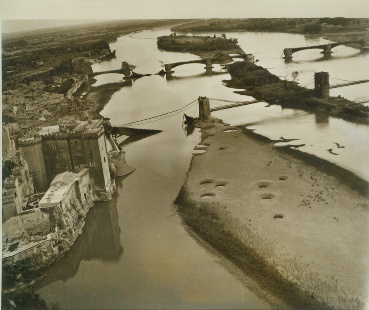 To Help Free France, 9/9/1944. FRANCE -- Desolation marks the once beautiful Rhone River at Tarascon in Southern France. Wrecked bridges, effectively bombed by the Allies to hinder the German retreat, are a grim reminder of the destruction that accompanies war. Pock marks in the islets between bridges show where Allied bombs missed their target. At left is a castle-like building one of many that dot the countryside in Southern France. Photo by Charles Seawood, ACME Photographer for the War Picture Pool. Credit - WP- (ACME);