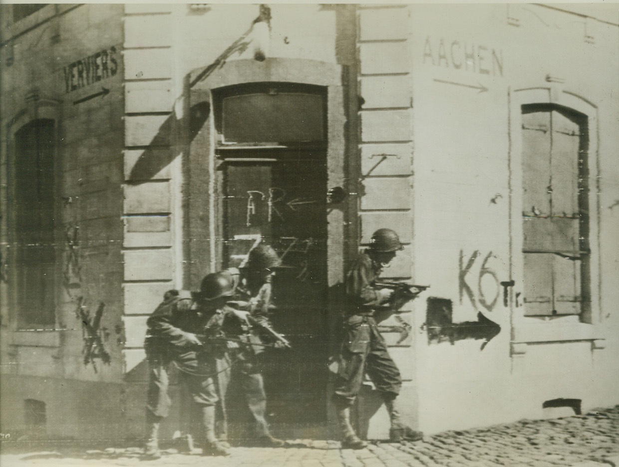 Caution Makes for Success, 9/14/1944. THIMISTER, BELGIUM -- Peering cautiously around the corner of this building, a three-man combat patrol scouts out the little town of Thimister. They are moving in advance of the main forces. Note the sign on the building which points to Aachen.  Credit (Signal Corps Radiotelephoto from ACME);